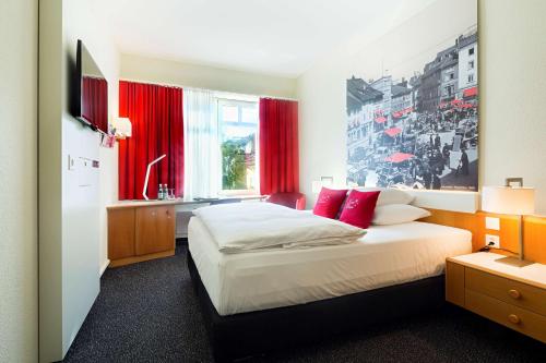 a bedroom with a large bed with red curtains at Hotel Wartmann am Bahnhof in Winterthur
