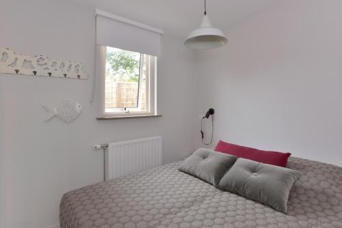 a white bedroom with a large bed with a red pillow at Banjaard Beachhouse Patrijzenlaan 14 in Kamperland