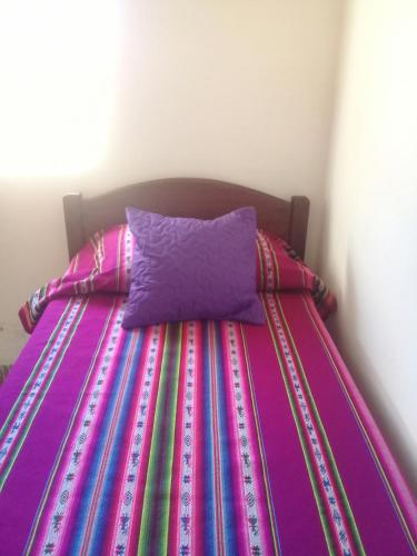 a bed with a colorful striped comforter and a purple pillow at Cabaña El Cardón,casita en el campo quebradeño in Humahuaca