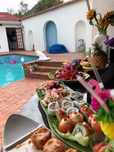 a table topped with plates of food next to a pool at Anoud Manor in Hout Bay