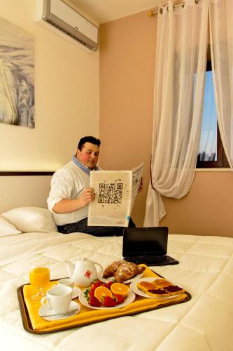 a man sitting on a bed reading a paper with a tray of food at Rifugio Delle Grotte in Castellana Grotte