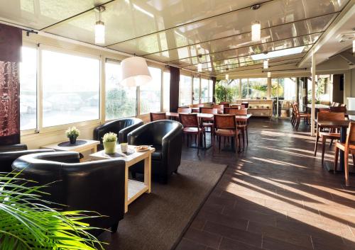 a restaurant with black chairs and tables and windows at Kyriad Caen Sud in Ifs