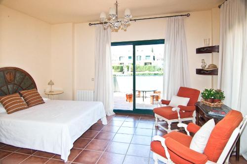 a bedroom with a bed and two chairs and a balcony at The Fairway Vista, Your Luxury Retreat with a Quiet Pool in Pueblo Nuevo de Guadiaro