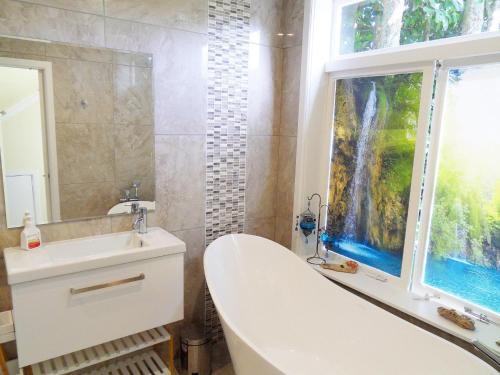 baño con bañera, lavabo y ventana en Atahu Cottage, en Omiha