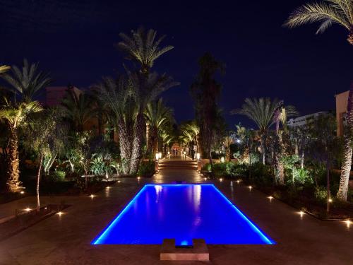 a pool with blue lights in a courtyard with palm trees at Mövenpick Hotel Mansour Eddahbi Marrakech in Marrakech