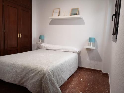 a small white bedroom with a bed and two lights at Apartamentos nueva 13 in Ronda