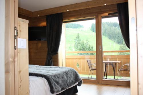 a bedroom with a bed and a balcony with a table at Hôtel Restaurant "Les Sapins" Wellness & Gourmet in Manigod