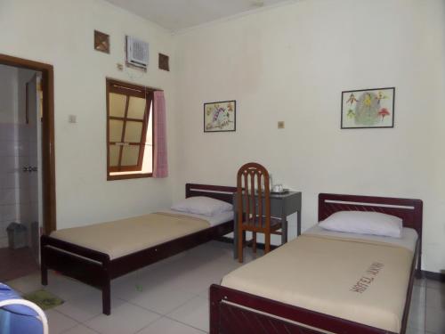 a room with two beds and a chair and a table at Armi Hotel Malang in Malang