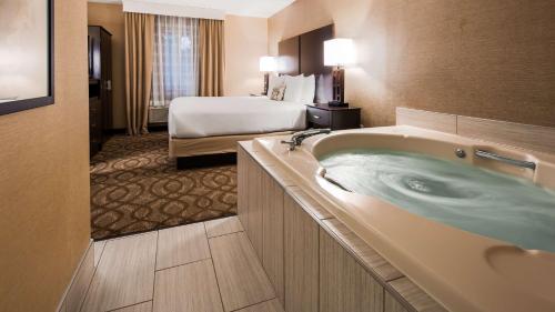 ein Hotelzimmer mit einer Badewanne und einem Bett in der Unterkunft Best Western Okemos/East Lansing Hotel & Suites in Okemos