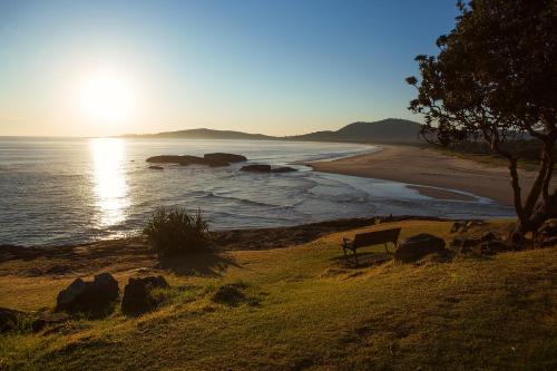 a bench sitting on the side of a beach at Horseshoe Bay Holiday Park in South West Rocks