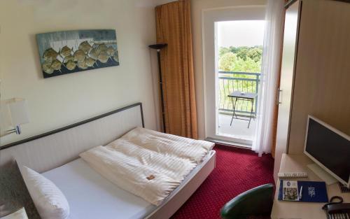 um quarto com uma cama, uma televisão e uma janela em Parkhotel Neubrandenburg em Neubrandenburg