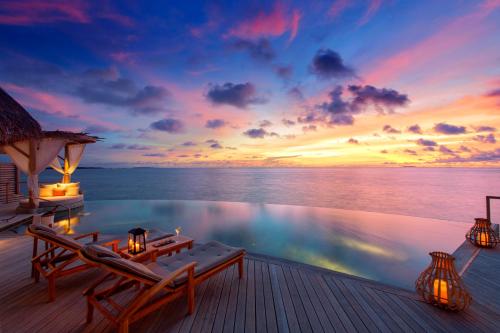 a pool on the deck of a resort with a sunset at Milaidhoo Maldives in Baa Atoll
