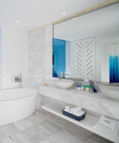 a white bathroom with two sinks and a large mirror at Mykonos Grand Hotel & Resort in Agios Ioannis Mykonos
