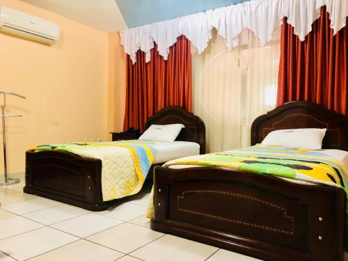 two beds in a room with red curtains at D'ORLAND HOTEL in Santo Domingo de los Colorados