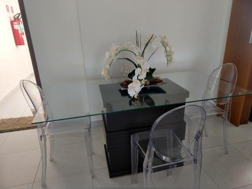 a glass table with two chairs and a vase with flowers at Essencial Manaíra in João Pessoa