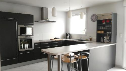 une cuisine avec des placards noirs et un îlot de cuisine avec des tabourets dans l'établissement Maison lumineuse, aux Herbiers