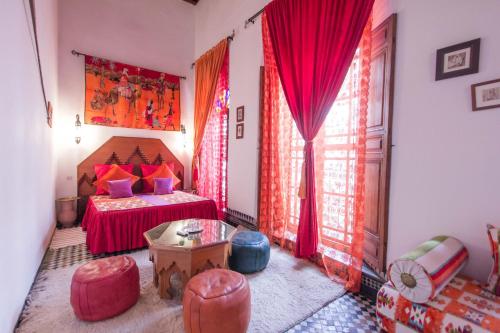 a bedroom with a bed with red curtains and a table at Riad Dar Skalli & SPA in Fès
