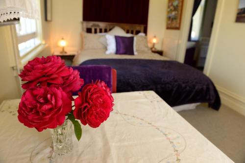a vase with red flowers on a table in a bedroom at Laurel Bank House in Queenstown