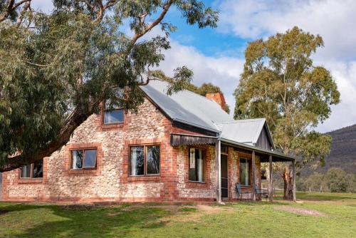 una vieja casa de ladrillo en un campo de hierba con un árbol en Grampians Pioneer Cottages, en Halls Gap