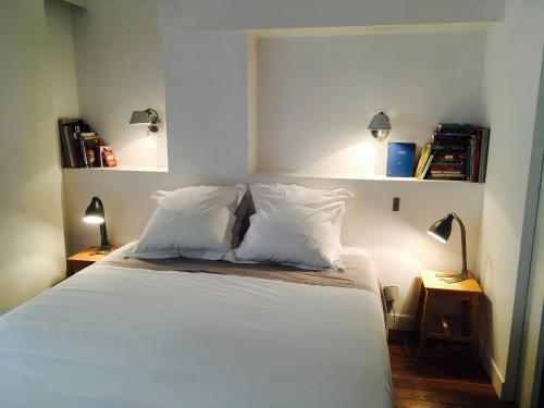 una camera da letto con letto, lenzuola e cuscini bianchi di Chez Vous ST HONORÉ a Parigi