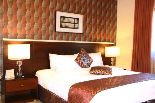 a bedroom with a bed with two lamps and a wall at City Rose Hotel Suites in Amman