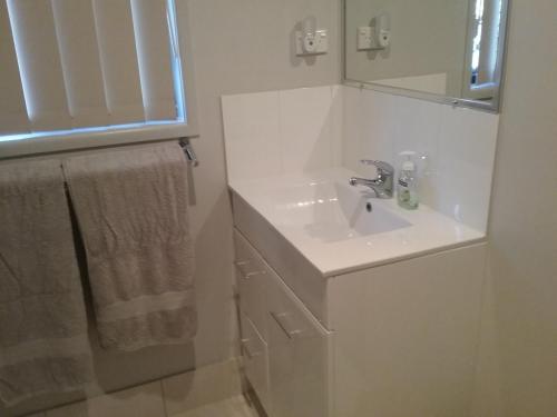 a white bathroom with a sink and a mirror at Banksia Apartment in Maryborough
