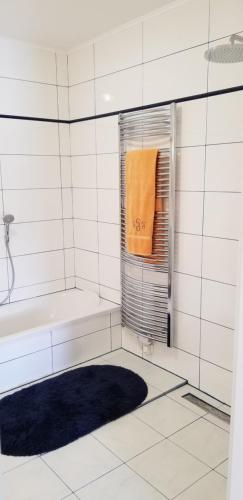 ein weiß gefliestes Bad mit einer Badewanne und einem orangenen Handtuch in der Unterkunft Haus Falkenstein in Moosburg