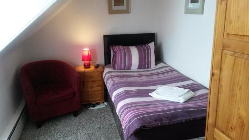 a small bedroom with a bed and a red chair at Station View Guest House in Dyce