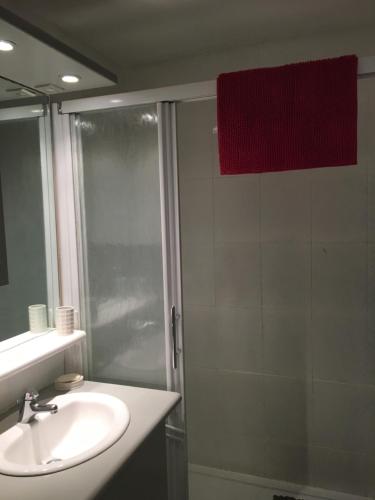 La salle de bains est pourvue d'un lavabo, d'une douche et d'une serviette rouge. dans l'établissement "Le Pharo" 17 Impasse du globe Appartement, au Cap d'Agde