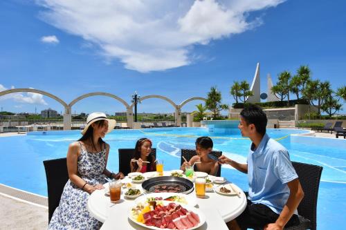 a family sitting at a table in front of a pool at Loisir Hotel Naha in Naha