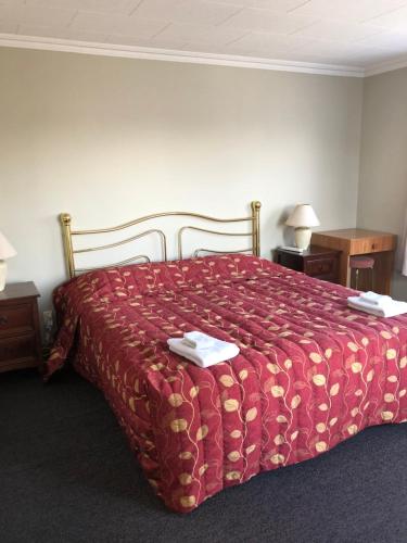 a bedroom with a bed with a red comforter at Lilybrook Motel in Rangiora