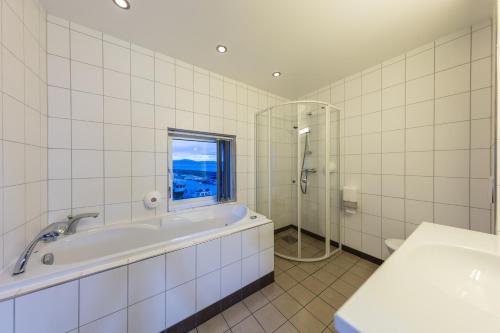 uma casa de banho em azulejos brancos com uma banheira e uma janela em Ørland Kysthotell em Brekstad