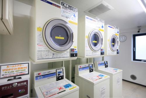 a laundry room with three washing machines and posters at Smile Hotel Tokyo Ayase Ekimae in Tokyo