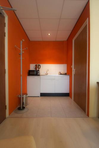 a kitchen with orange walls and a white counter at De Kapschuur in Stadskanaal