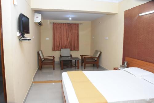 a hotel room with a bed and chairs and a television at Hotel Surya Residency Majestic in Bengaluru