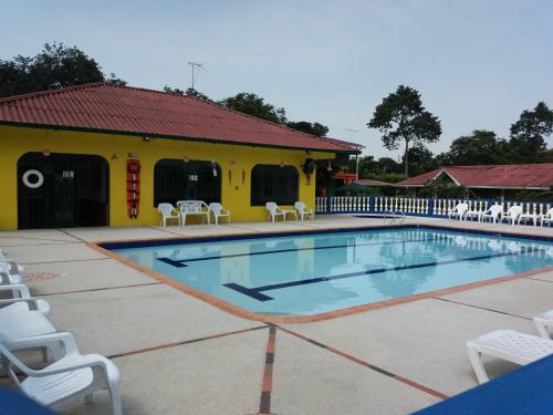 uma piscina com cadeiras brancas e um edifício amarelo em Finca Las Orquideas em La Horqueta