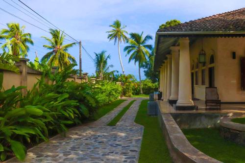 a house with a walkway next to a house with palm trees at Heenatigala Walawwa in Talpe