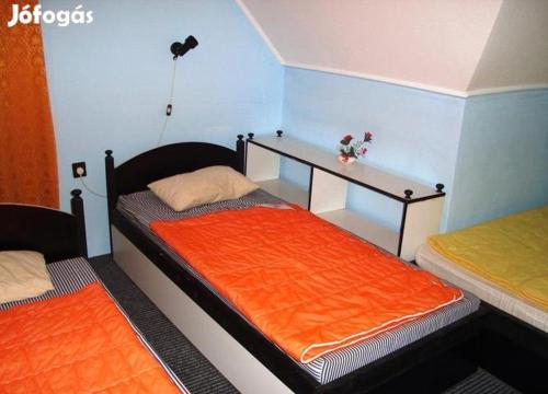 ボガーチにあるVica Vendégházのベッドルーム1室(オレンジのシーツと棚付きのベッド2台付)