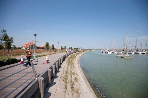 Una mujer y dos niños caminan por un paseo marítimo junto al agua. en Duinenblik 3, en Nieuwpoort