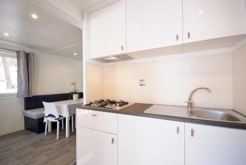 a kitchen with white cabinets and a sink and a table at Camping Village Le Calanchiole in Capoliveri