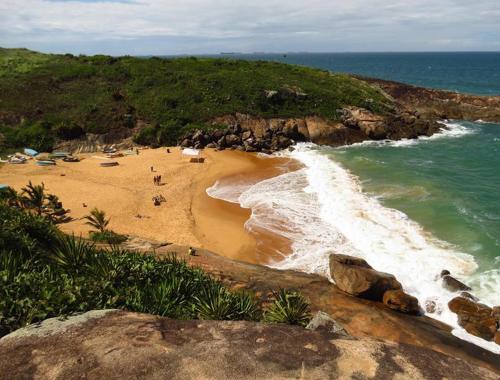 a beach with people on the sand and the ocean at Vila Suítes Coliving in Vila Velha