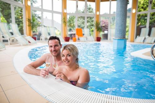 Ein Mann und eine Frau im Schwimmbad mit einem Glas Wein. in der Unterkunft Hotel Trattnig in Döbriach
