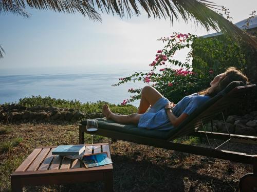 a woman laying in a chair looking at the ocean at Dammuso sulla scogliera - Pantelleria in Scauri