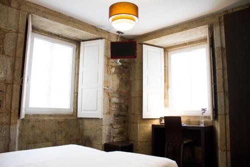 a bedroom with two windows and a bed and a desk at Hotel A Tafona do Peregrino in Santiago de Compostela