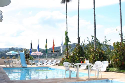 einen Pool in einem Hotel mit Stühlen, Tischen und Sonnenschirmen in der Unterkunft Hotel Dominguez Master in Nova Friburgo