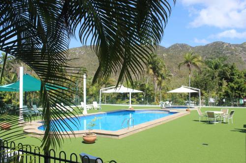 a beach area with a pool, lawn chairs, and a tennis court at Amaroo On Mandalay in Nelly Bay