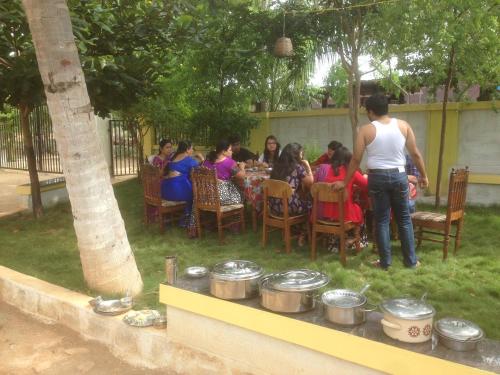 a group of people sitting at a table in a garden at Holiyday in VGF Farm House in Dānishpet