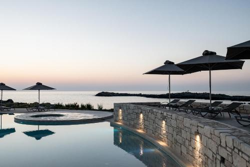 a swimming pool with umbrellas and chairs next to the water at Kavos Hotel & Suites in Stavros