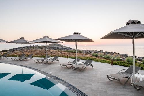 a pool with chairs and umbrellas next to the ocean at Kavos Hotel & Suites in Stavros
