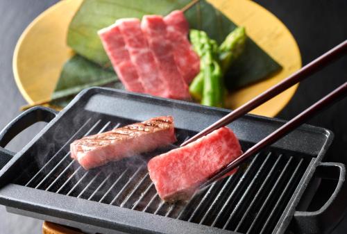 two pieces of meat are cooking on a grill at Honjin Hiranoya Kachoan in Takayama